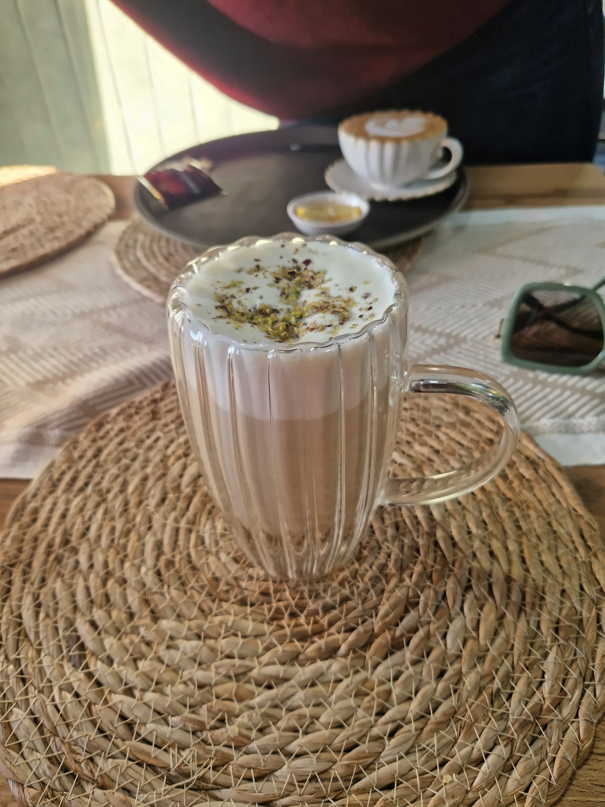 A latte in a glass cup on a woven mat